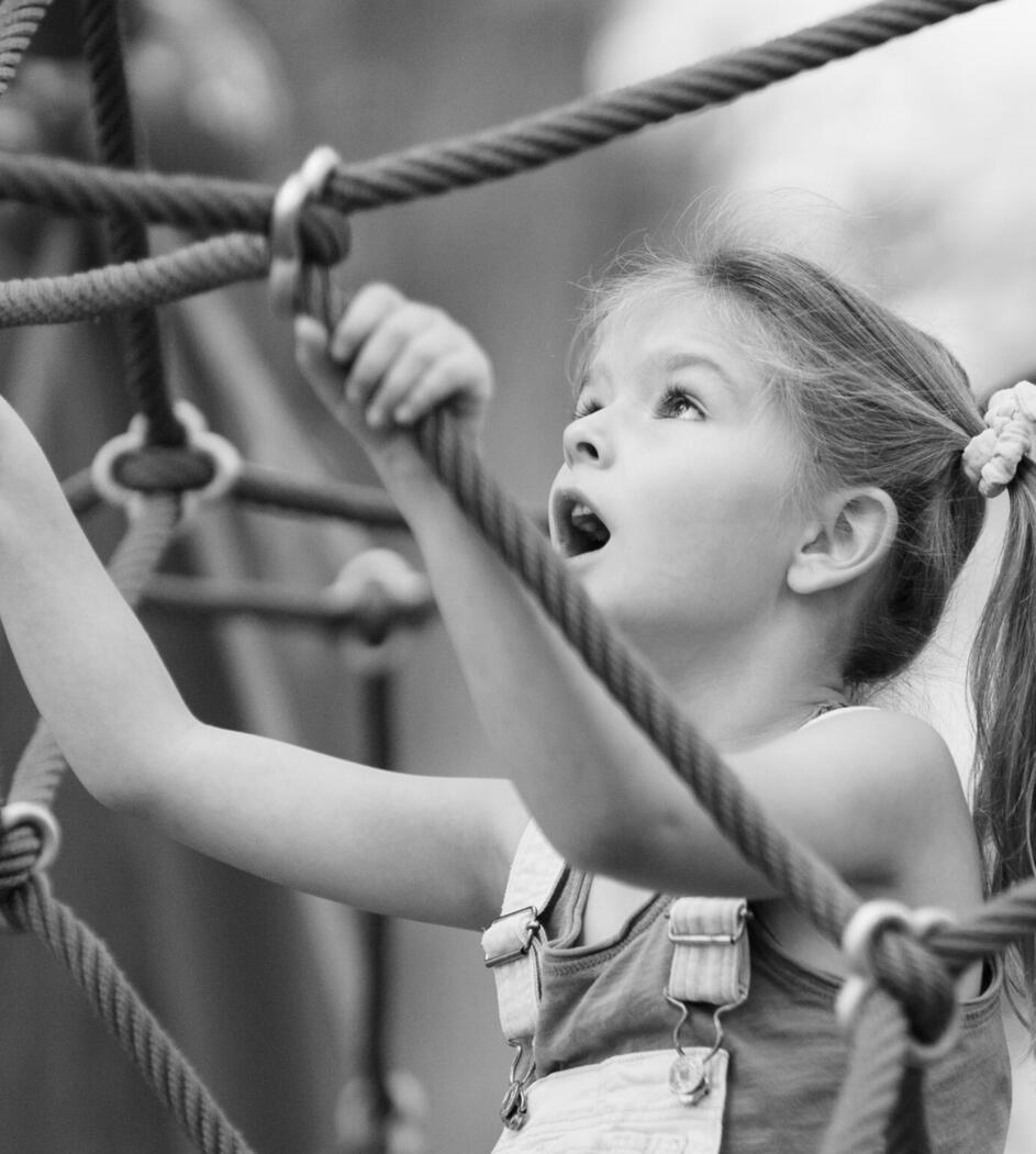 A child looks up while climbing a rope playground